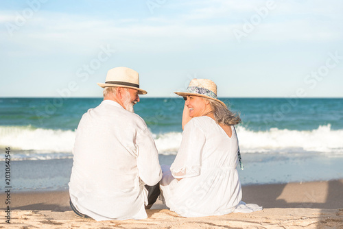 Картината върху платно Happy senior couple sitting on beach enjoying time together during summer vacati