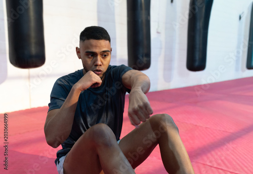 Valokuva Man wearing athletic shorts sitting on red mat performing situp-punch in boxing