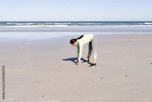 Canvastavla Asian woman bending reaching for shells on beach wearing longsleeve top leggings