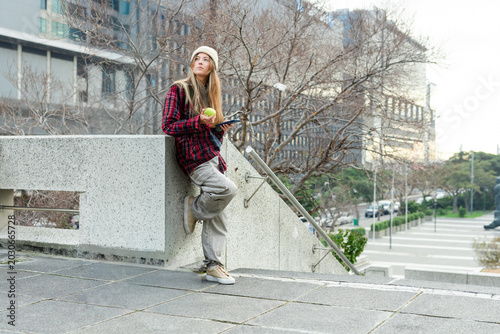 Photos Woman leaning on parapet in urban plaza, wearing plaid jacket, with green apple