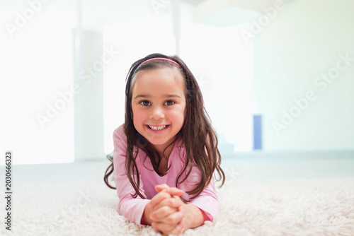 Female child lying on plush white rug in room with large windows wearing pink headband top