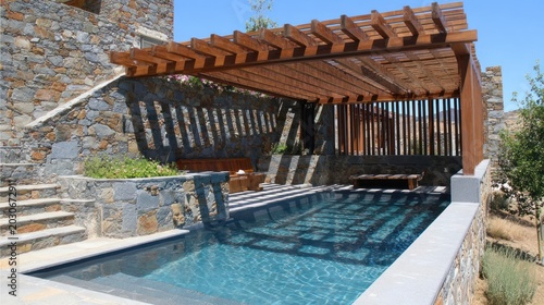 Rustic outdoor swimming pool area features a wooden pergola casting striped shadows on the water