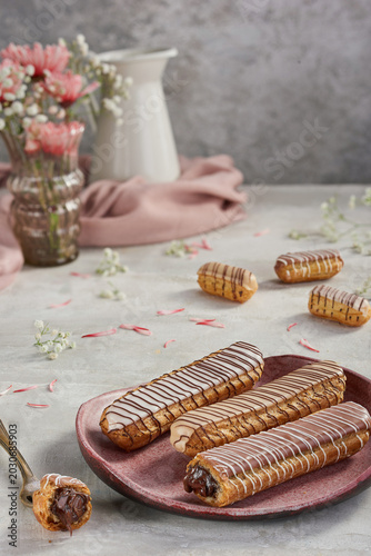 fresh French eclairs filled with rich chocolate cream, beautifully drizzled with dark and white chocolate stripes on a ceramic plate, featuring mini eclairs and elegant floral decorations.