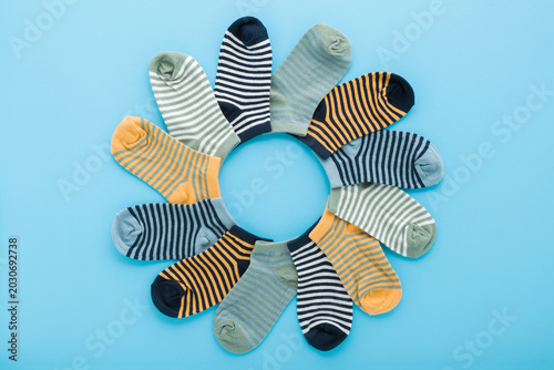 Created circle shape from new colorful striped short socks for little child boy on light blue table background. Pastel color. Closeup. Flat lay. Top down view.