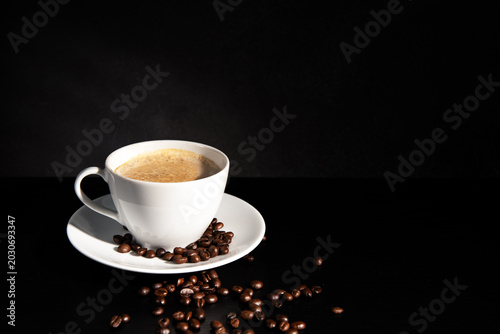 Premium dark roast arabica coffee beans with cozy cup of warm steaming coffee and sugar on dark background with copy space