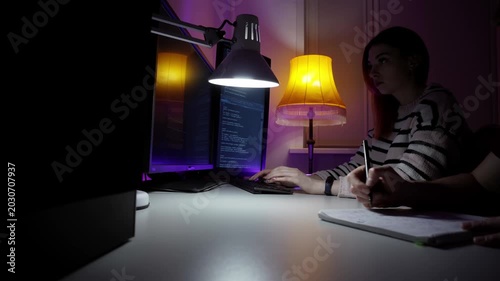 Senior developer mentoring junior at monitors, hands on keyboard with purple studio lighting, live code review and feedback session with notebook, lamp and focused learning atmosphere.