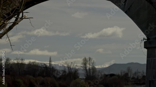 Stone bridge arch framing a scenic landscape with snow capped mountains
