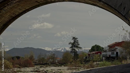 Looking through an ancient stone bridge arch at the dry riverbed