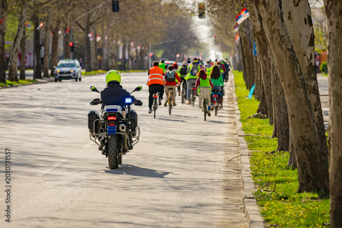 Police officer on motorcycle secures group of cyclists on city road, street, asphalt