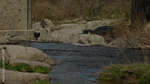 River stream flowing through rocky terrain and past a stone bridge pier with ...