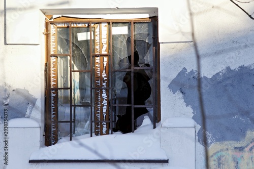 Fotografija A stark winter scene featuring a broken window pane on a weathered wall heavily