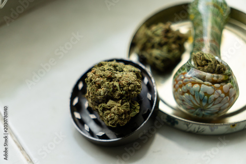 Fotografia Overhead view of a large dry weed bud, an open metal grinder, and a glass smoking pipe inside a stash tin