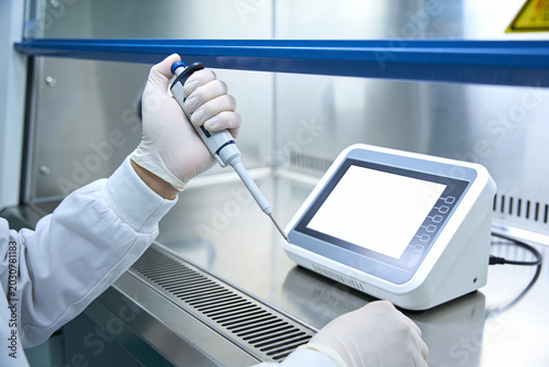 Foto Scientist in sterile lab coat and gloves uses pipette with digital device