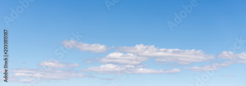 Clear blue sky with scattered white clouds across a calm summer horizon backg...