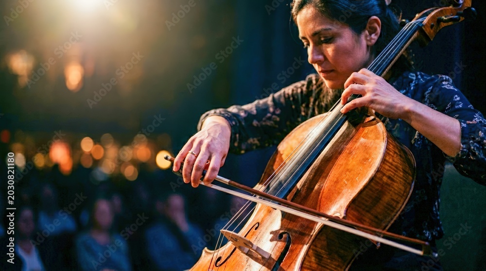 Fototapeta premium Woman playing cello on stage with audience in background.