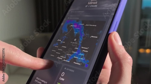 Hands swipe smartphone weather app in a home interior. Forecast maps and temperatures scroll on the screen. Mobile climate checking for daily planning and travel..