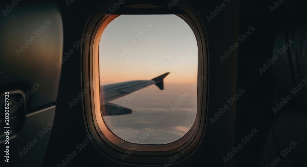 Fototapeta premium Airplane window view of wing during sunset with clouds below.