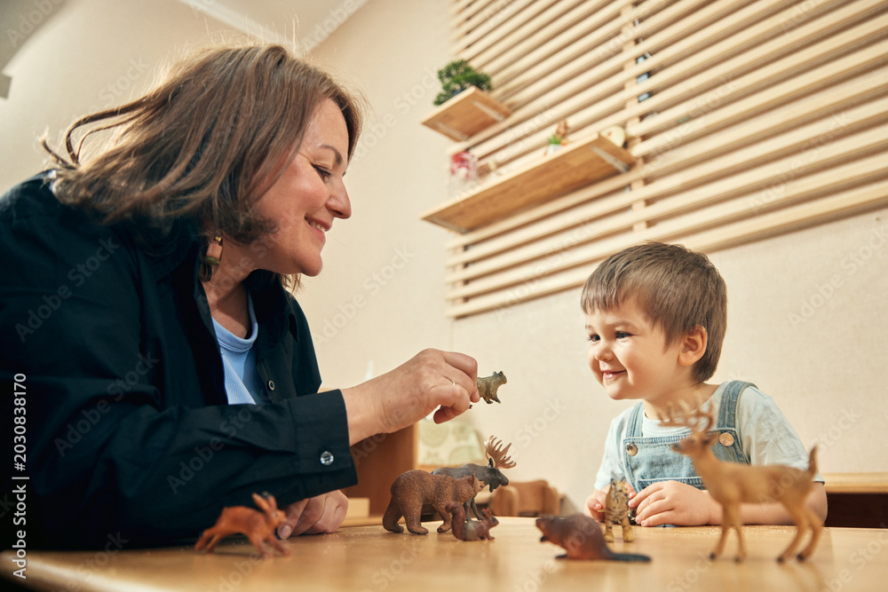 Fototapeta premium Happy boy learning animal names through play with caring preschool educator. Concept of speech development, animal vocabulary, emotional connection, childcare therapy, and early education.