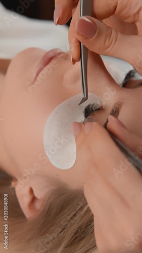 A skilled beautician carefully applies eyelash extensions to a client using tweezers, focusing on detail and hygiene. The process highlights modern beauty trends and salon expertise