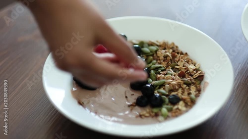 Hand adding fresh berries into healthy yogurt granola bowl close up breakfast preparation video