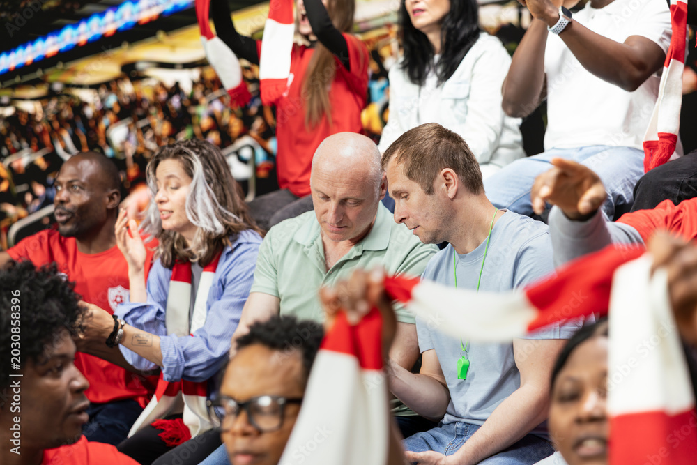 Fototapeta premium Football fans placing a risky bet ticket on in-play live gambling app, watching intense soccer match from the stadium stands. Enthusiasts follow sports betting odds during important game.