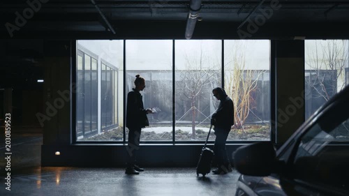 Two shadowy figures meet between parked cars at night, exchanging a suitcase for a thick envelope of money. 