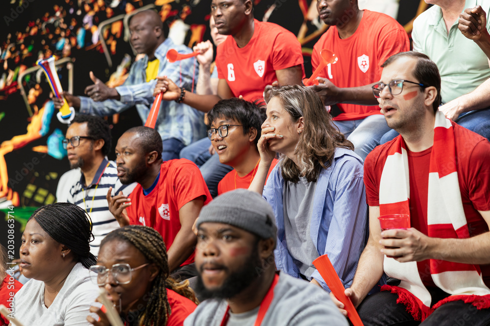 Fototapeta premium Red team football supporters watching tense live soccer match from stadium stands, mixed emotions, horns and anxious crowd reaction. Sports fans clenching fists speechless after missed goal.