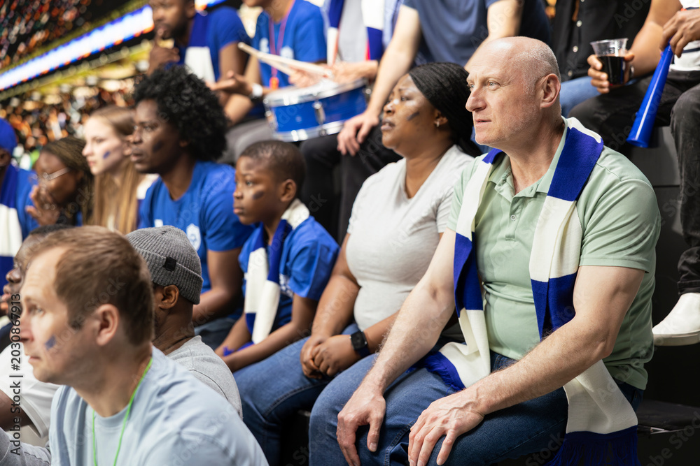 Naklejka premium Tense blue team supporters reacting to close call during soccer match in a crowded stadium, wait for final whistle. Multigenerational supporter group show suspense and anticipation.