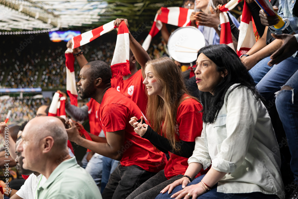 Fototapeta premium Focused football supporters watching dramatic final minutes of a soccer match filled with suspense and tension. Sports fans asking for the final whistle in the stadium, speechless after close call.