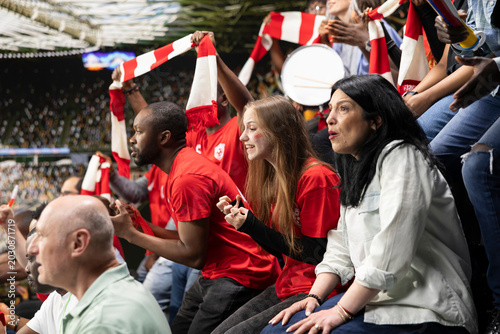 Schilderij op canvas Focused football supporters watching dramatic final minutes of a soccer match filled with suspense and tension