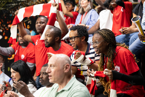 Photos Female soccer fans celebrating goal with raised arms in crowded stadium stands, red team supporters and energetic live match atmosphere in fan section