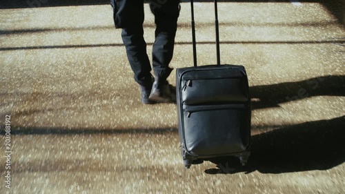 Mysterious man in black clothes pulling a suitcase through a sunlit modern underground parking