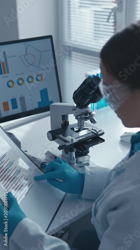 Woman researcher in lab coat examines samples under microscope, reviewing statistical charts on tablet. Laboratory environment highlights scientific progress and digital data integration