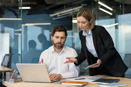 Photos Two business professionals in an office environment discussing a project, with t