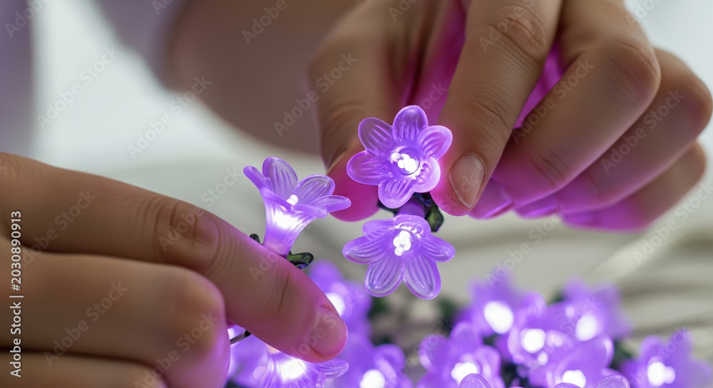 Fototapeta premium Hands arranging purple flower-shaped string lights indoors 