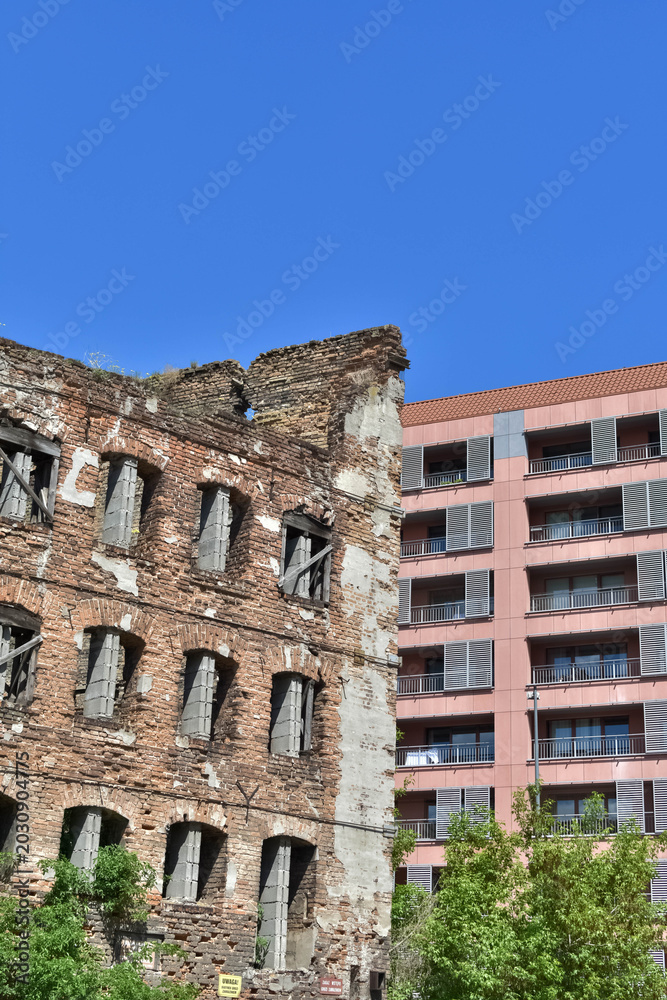 Obraz premium Ruins of an old red brick building standing next to a modern residential apartment house. Contrast of historical and contemporary urban architecture. 