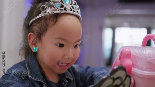Фотография A curious toddler girl plays dress-up with a tiara and glitter makeup, exploring her imagination and developing self-expression while playing indoors