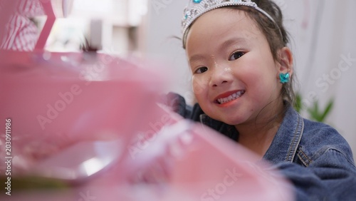 Fotografie A happy young girl wearing a princess tiara and makeup smiles at the camera while playing dress-up, expressing her childhood imagination and joyful creativity at home