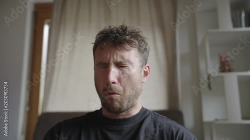 Caucasian man sitting at home eating a very sour candy, making a funny face of disgust and distaste