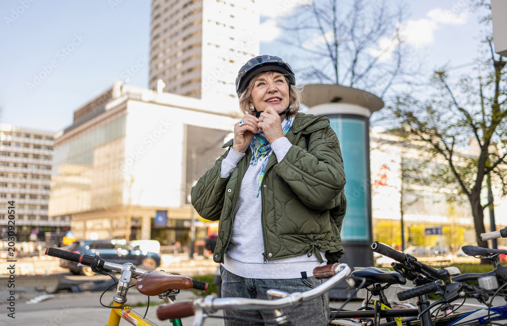 Fototapeta premium Senior woman wearing helmet while riding bicycle in the city 