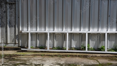 Obraz na płótnie Horizontal shot of a lightweight aluminum metal ladder laying down on a concrete floor ground surface against a weathered gray corrugated steel zinc sheet wall panel background