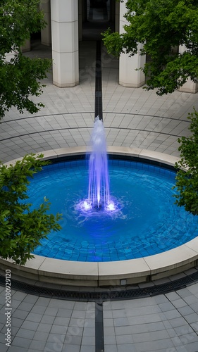 Serene fountain with purple lights surrounded by trees and a stone walkway in a public plaza