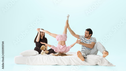 Canvastavla Parents playing with daughter doing upside down trick on white bed in pastel studio