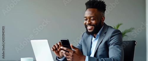 Happy African business man employee student looking away using smartphone at work smiling young adult male professional worker holding cell phone smart mobile tech working in office sitting at desk co