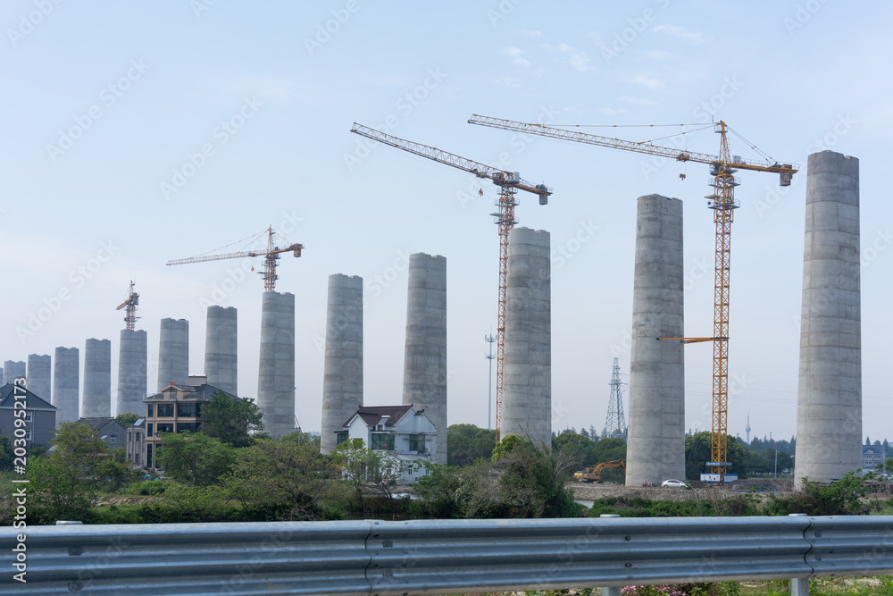 Fototapeta premium massive concrete bridge piers and yellow tower cranes at highway construction site
