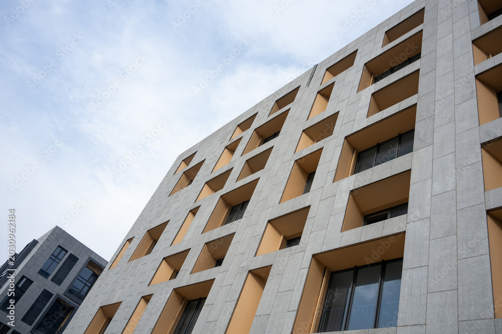 Fototapeta premium Modern building facade featuring geometric windows and stone texture against blue sky