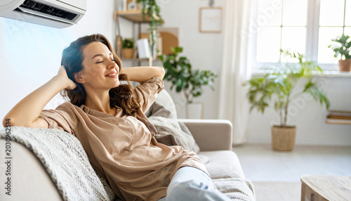 Young Woman Relaxing on Sofa Enjoying Cool Air from Air Conditioner