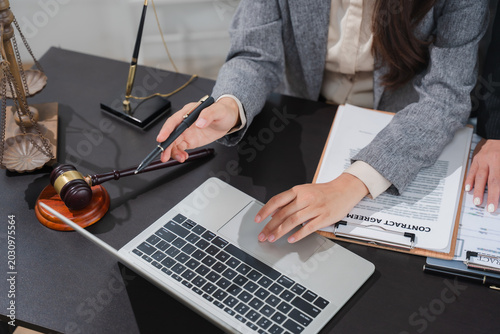 Legal Consultation: A close-up shot shows a legal professional using a laptop, with a gavel, scale of justice, and contract agreement on the desk, symbolizing legal proceedings and advice.
