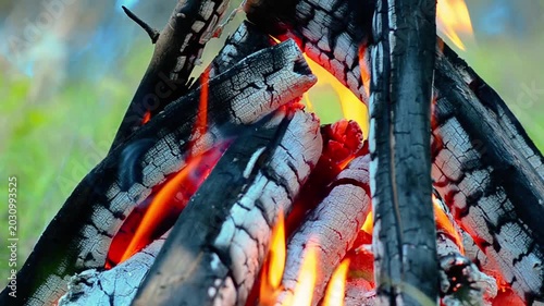 Macro shot of glowing embers and charred wood logs in burning campfire, cinematic close up of hot bonfire texture with orange coals and soft smoke rising outdoors, cozy autumn camping concept in 4K