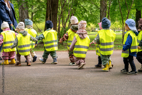 Kindergarten teacher leading a group of children in yellow safety vests walking in line with a safety rope